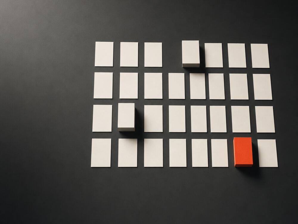 A precise grid of blank cards seen from above, three raised on risers and one of them signal orange.