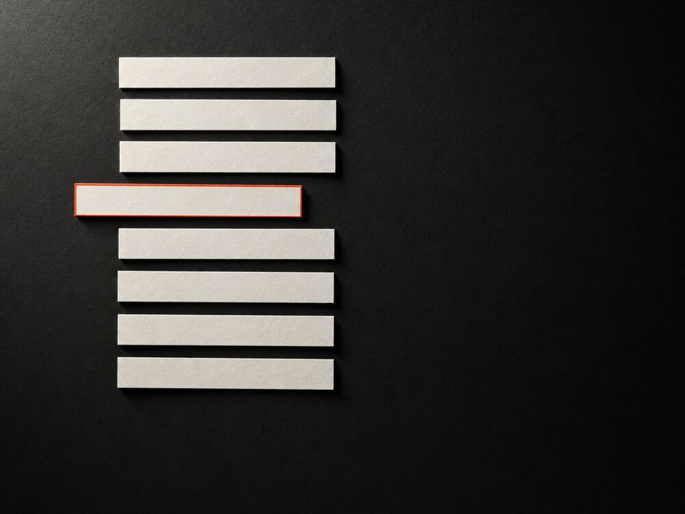 Narrow blank paper strips stacked like subtitle lines, one shifted out of rhythm and edged in orange.